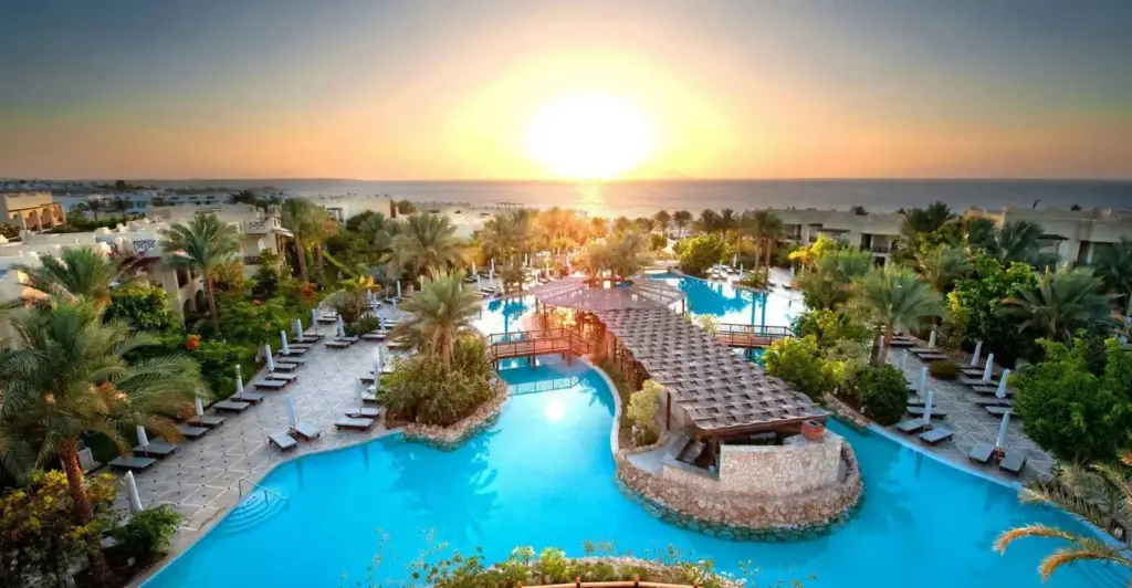 Тихий курортный комплекс на закате с бассейнами и видом на море, создающий общее представление о погоде в Египте в тёплый сезон.
