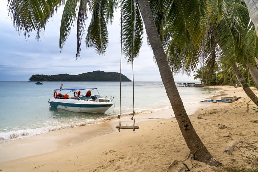 Чартерные и регулярные рейсы: что выбрать для тура — пляж с пальмами, качелями и лодкой у берега, как иллюстрация спокойного отдыха и планирования перелёта