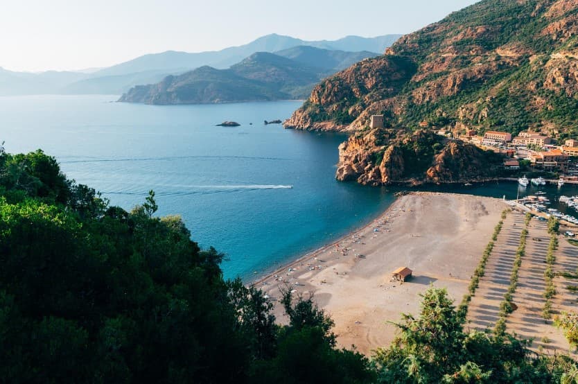 Чартерные и регулярные рейсы: что выбрать для тура — бухта с пляжем у скалистых гор и прибрежного городка, как иллюстрация планирования перелёта и отдыха