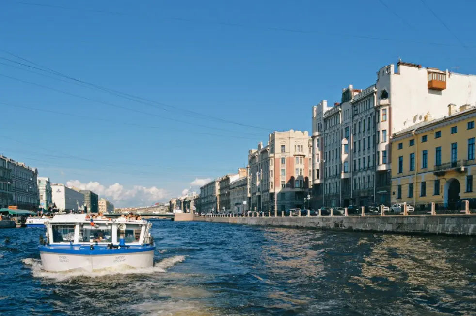 Лучшее время суток для экскурсии: утро/день/вечер — прогулочный катер на реке в городе, солнечный день и набережная с историческими зданиями.