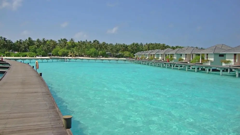 Страховка от невыезда: когда нужна и как работает — пирс над бирюзовой лагуной и бунгало на воде на курорте.