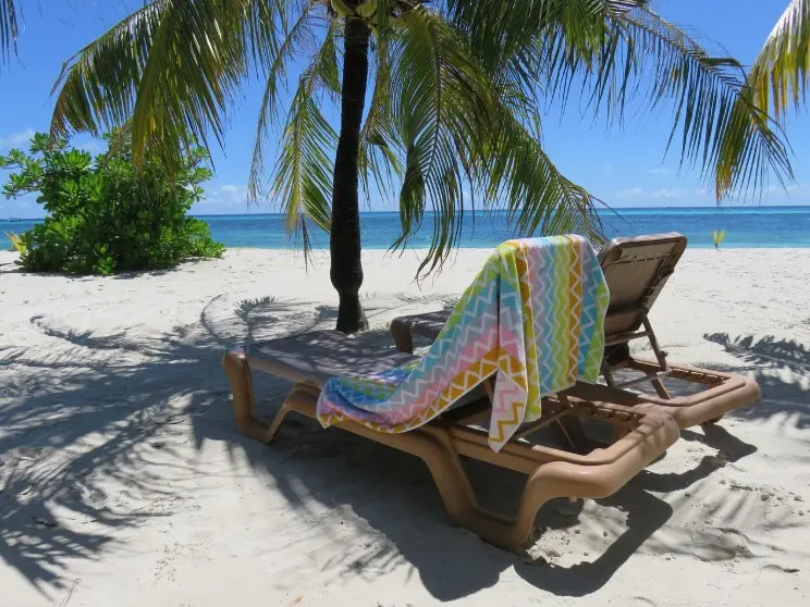 Страховка от невыезда: когда нужна и как работает — шезлонг под пальмой на белом пляже у моря, подготовка к отдыху.