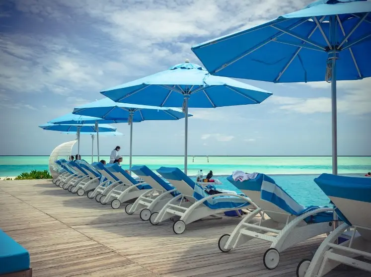 Страховка от невыезда: когда нужна и как работает — шезлонги у бассейна и голубые зонты на фоне моря, курортная зона отдыха.