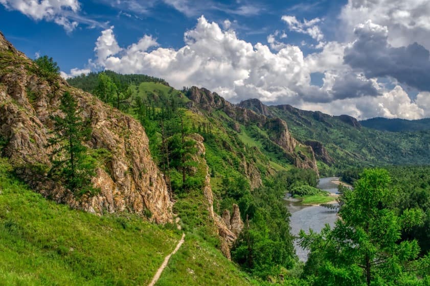 Экскурсии по России: горная долина с рекой, скалами и зелёными лесами под облачным небом
