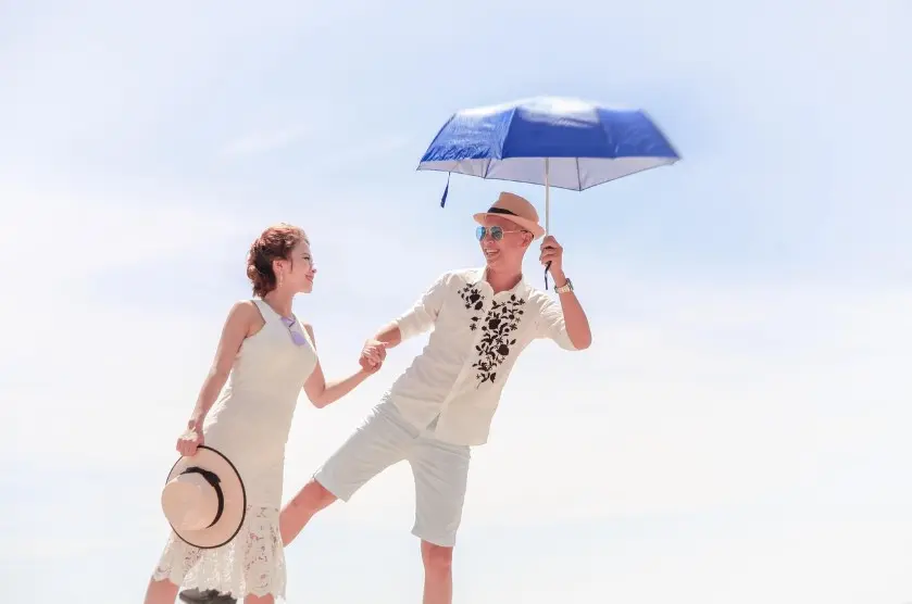 Где и как идеально провести медовый месяц: счастливая пара на пляже держится за руки под зонтом у моря